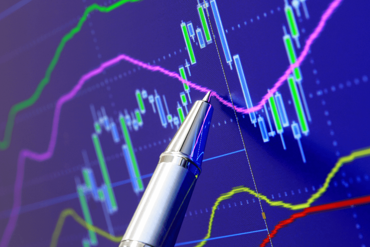 Caneta apontando para gráficos de desempenho financeiro em um monitor, ilustrando a solidez da Méliuz na bolsa de valores em comparação com concorrentes menores.