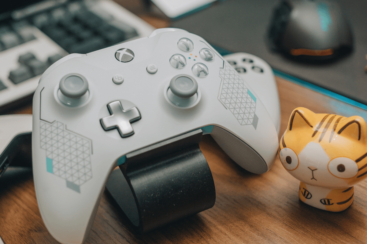 Controle de Xbox branco personalizado sobre uma mesa de madeira ao lado de uma miniatura, ilustrando como ganhar pontos no Microsoft Rewards jogando videogame.