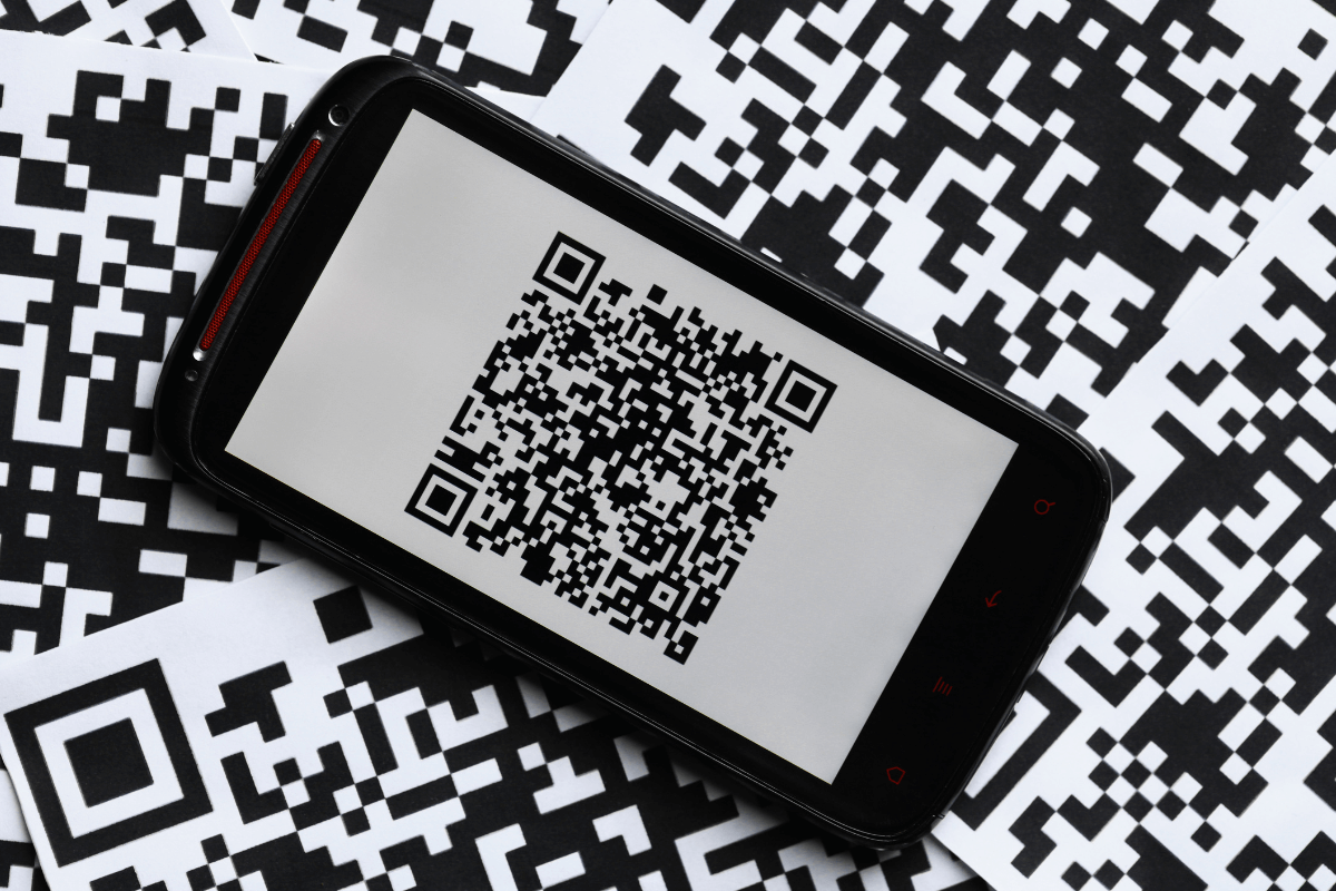 Smartphone exibindo um QR Code sobre um fundo com vários códigos misturados, ilustrando dificuldades de leitura e validação da nota fiscal no aplicativo.
