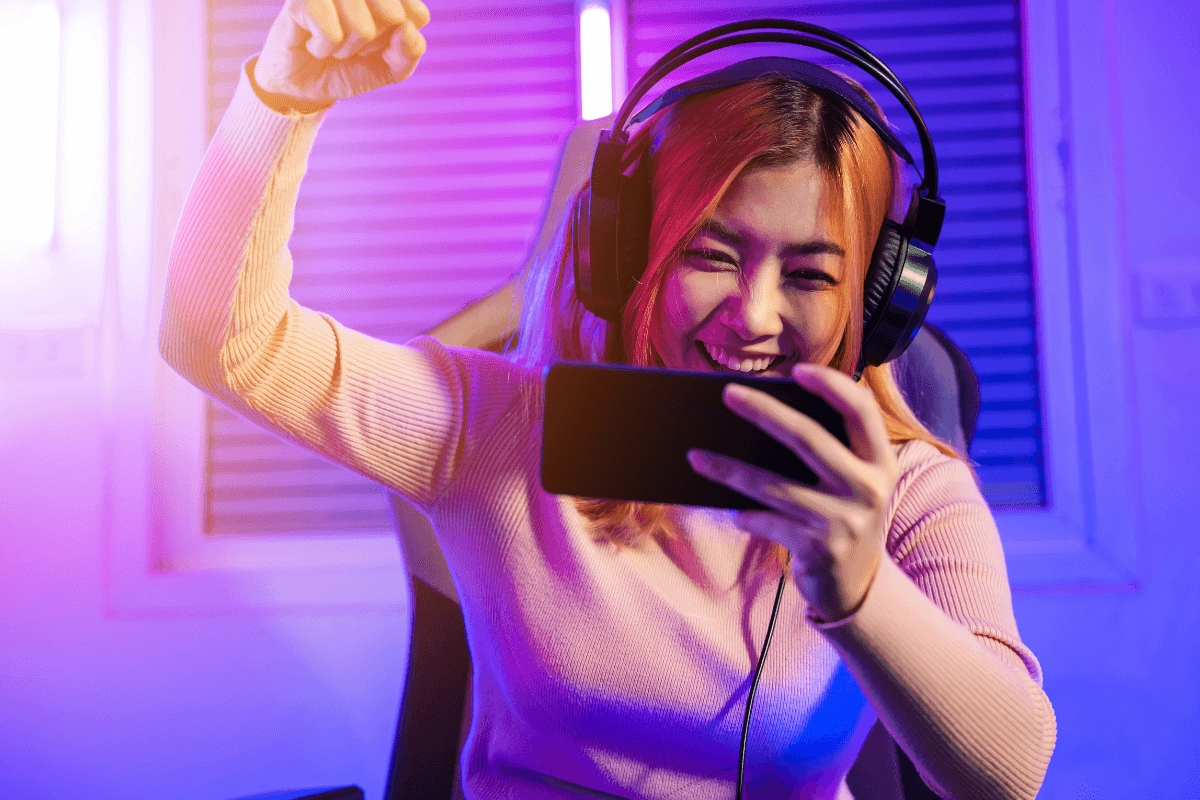 Jovem gamer sorrindo para o celular com iluminação neon, ilustrando a felicidade de resgatar recompensas de jogos com saldo do Microsoft Rewards.