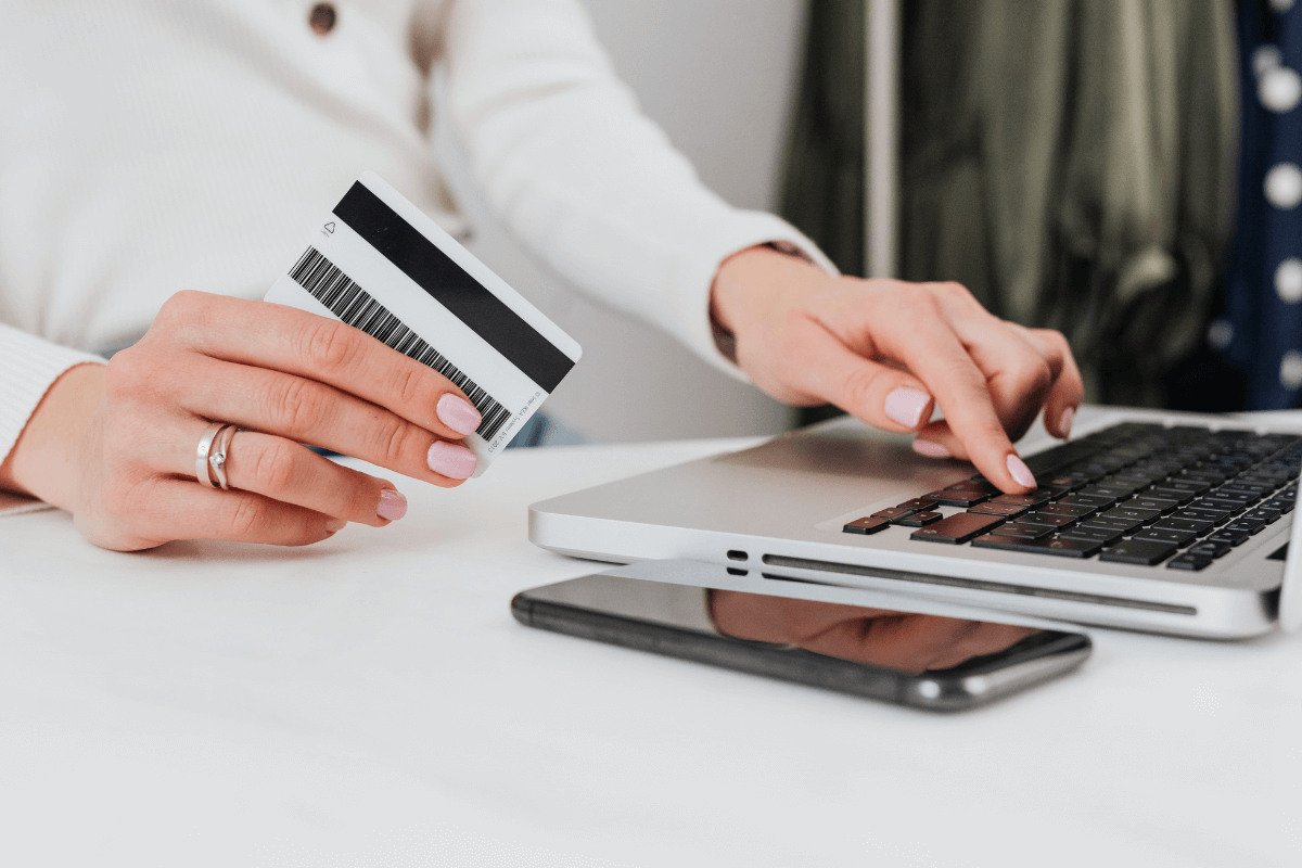 Detalhe das mãos de uma pessoa segurando um cartão de crédito e digitando em um notebook, ilustrando o processo de compra online que gera a comissão do cashback.