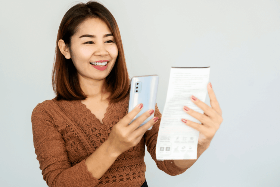 Mulher sorrindo segurando um smartphone e um cupom fiscal, ilustrando o que é o Méliuz nota fiscal e como ganhar dinheiro escaneando notas.