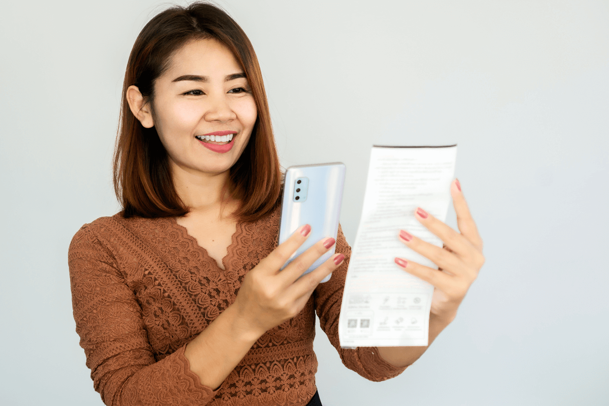 Mulher sorrindo segurando um smartphone e um cupom fiscal, ilustrando o que é o Méliuz nota fiscal e como ganhar dinheiro escaneando notas.