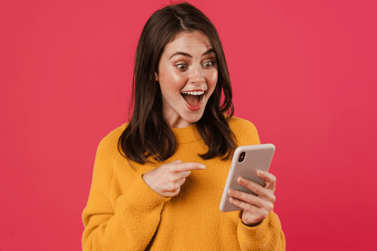 Mulher de blusa amarela apontando para o celular com expressão de surpresa e felicidade, ilustrando a confirmação de que o Ysense paga de verdade.