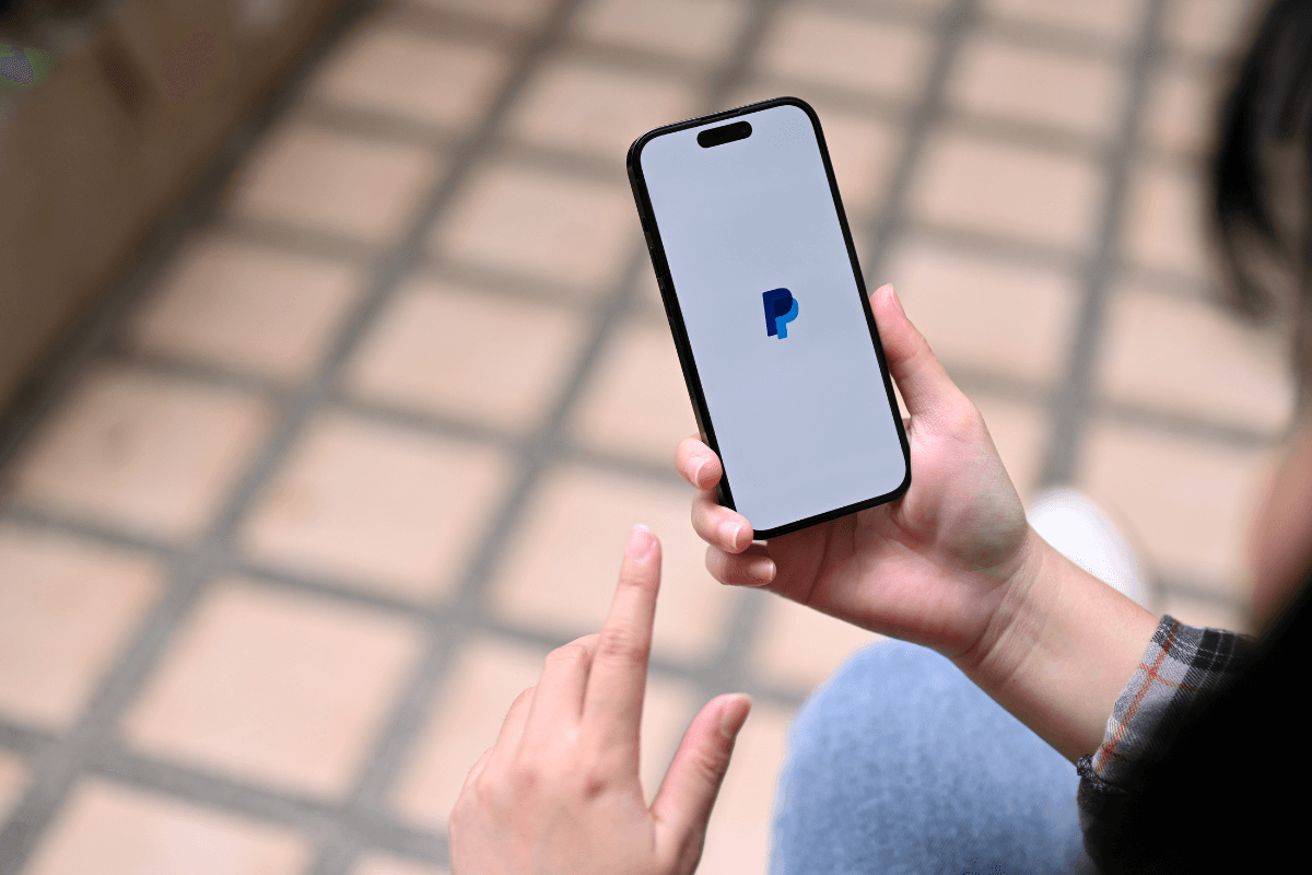 Mãos segurando um smartphone com o aplicativo do PayPal aberto na tela, ilustrando a principal carteira digital usada para receber pagamentos de pesquisas online com segurança.