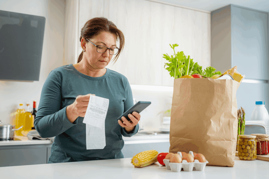 Mulher na cozinha usando o celular para escanear o QR Code da nota fiscal e ganhar dinheiro com aplicativos de cashback após as compras.