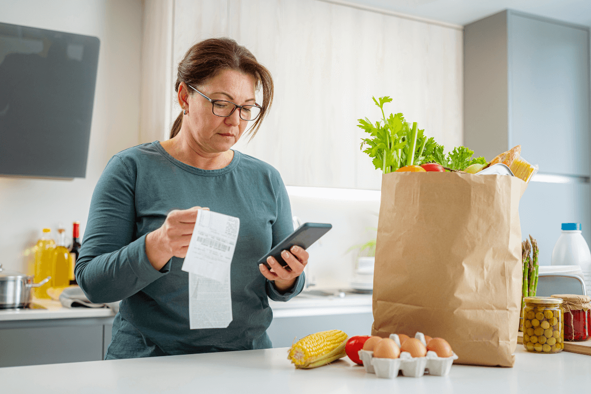 Mulher na cozinha usando o celular para escanear o QR Code da nota fiscal e ganhar dinheiro com aplicativos de cashback após as compras.