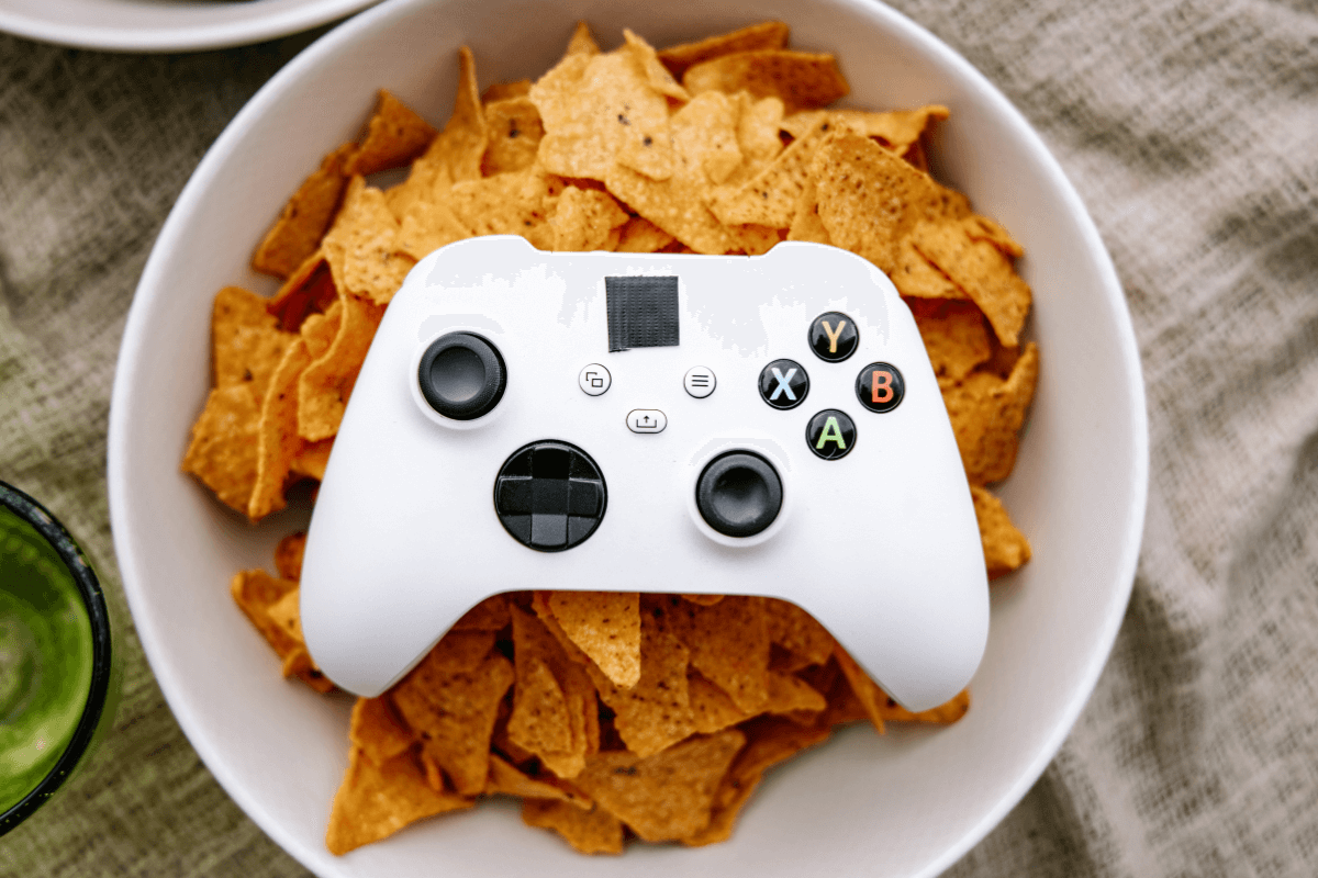 Controle de Xbox branco apoiado sobre uma tigela de salgadinhos, ilustrando como momentos de lazer podem virar saldo no Game Pass.