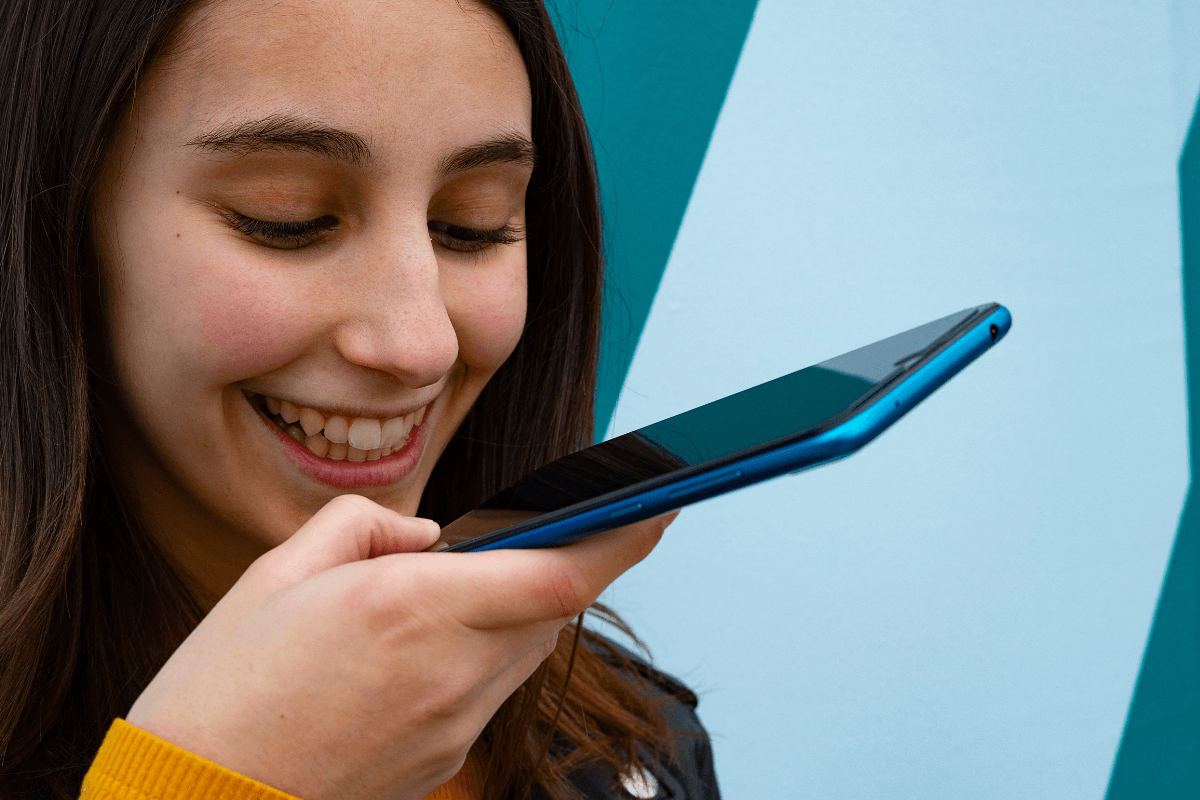 Jovem sorrindo enviando mensagem de áudio no celular, ilustrando estratégias de divulgação direta via WhatsApp e interação pessoal para fechar vendas como afiliado.