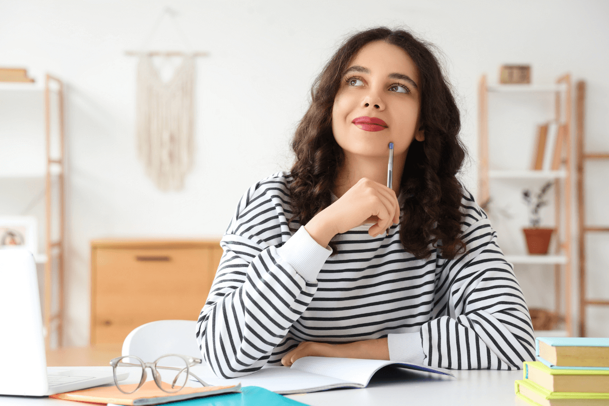 Mulher jovem pensativa em home office, segurando uma caneta e olhando para cima, ilustrando a dúvida comum de afiliados sobre onde divulgar seus links.