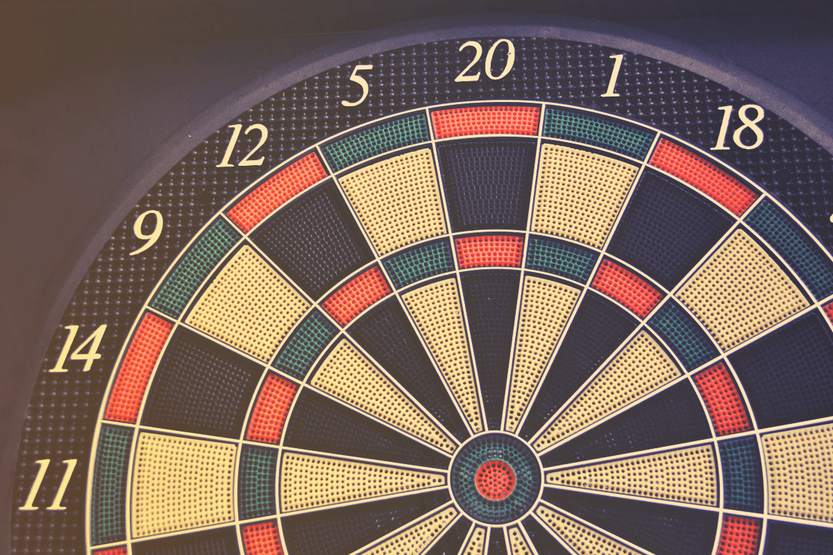 Close em um alvo de dardos colorido com números visíveis, simbolizando a precisão necessária para calcular o valor real de cada ponto antes da troca.