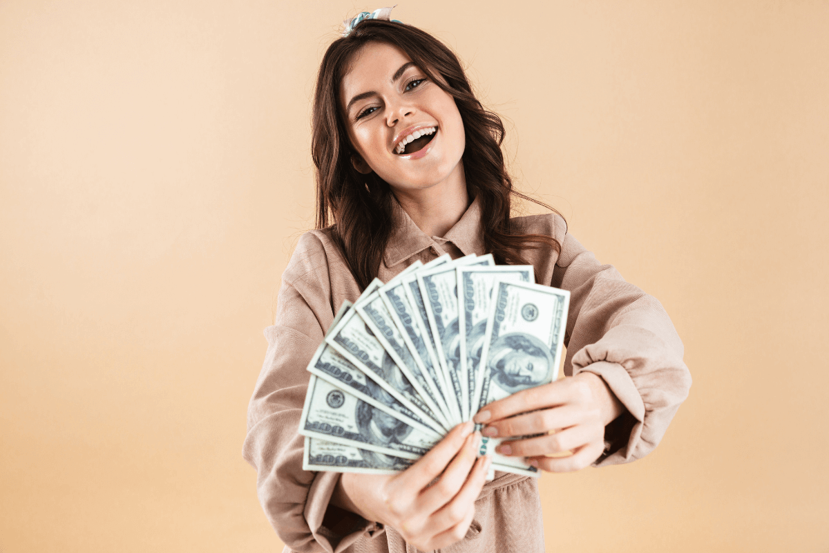 Mulher sorrindo segurando um leque de dinheiro, ilustrando o acúmulo de renda extra com estratégias de cashback.