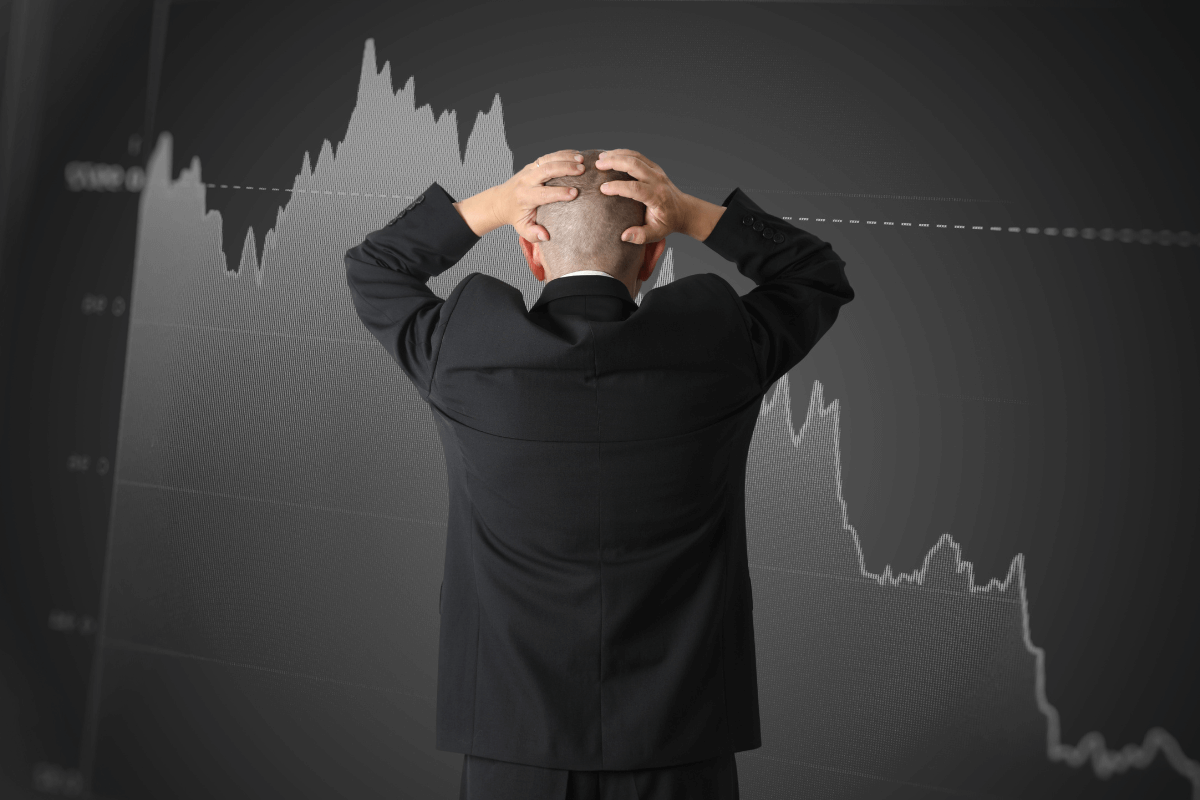 Homem de negócios com as mãos na cabeça em frente a um gráfico de queda, simbolizando a preocupação com riscos técnicos e a importância de estratégias de mitigação.