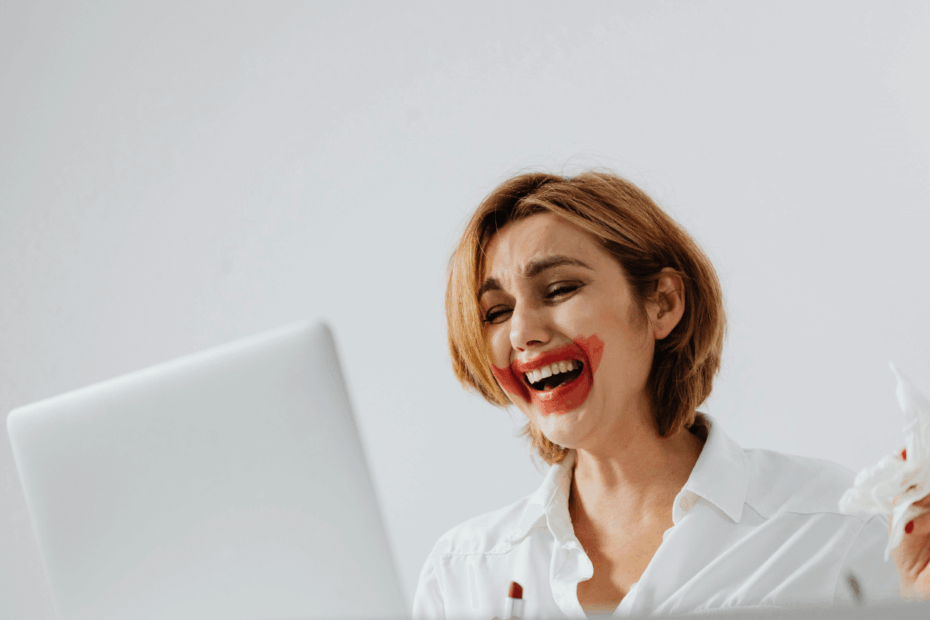 Mulher com a maquiagem borrada rindo de nervoso e chorando em frente ao notebook, ilustrando o desespero de quem acabou de descobrir na prática se os pontos Microsoft Rewards expiram.