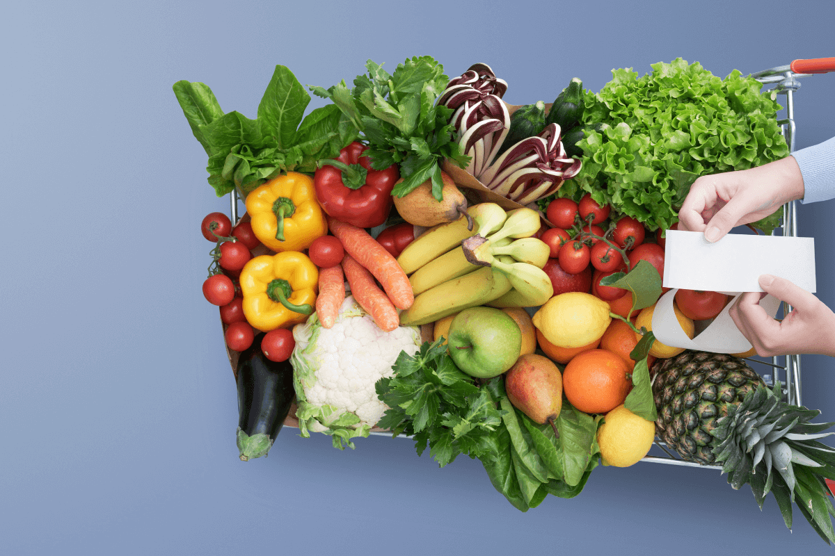 Carrinho de supermercado cheio de frutas e legumes com mãos segurando a nota fiscal, ilustrando como o perfil de consumo afeta os ganhos com QR Code.