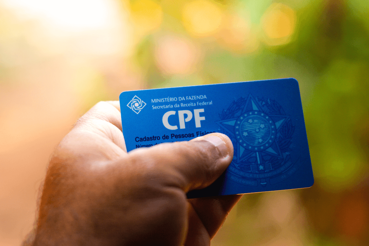Mão segurando um cartão azul de CPF brasileiro em foco, ilustrando o momento de cadastro e verificação de identidade em sites de pesquisa de mercado seguros.