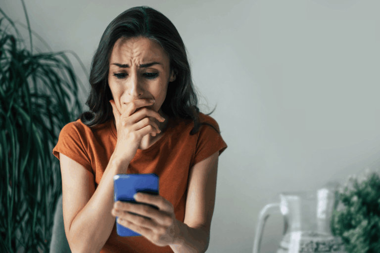 Mulher chorando com a mão na boca segurando o celular, representando a frustração de cair em golpes ao buscar sites que realmente pagam.